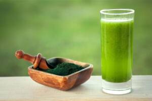 Ciotola contenente polvere di alga spirulina e un bicchiere di estratto