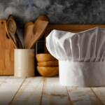 Cappello da chef con utensili da cucina in legno sullo sfondo