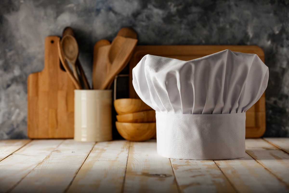 Cappello da chef con utensili da cucina in legno sullo sfondo
