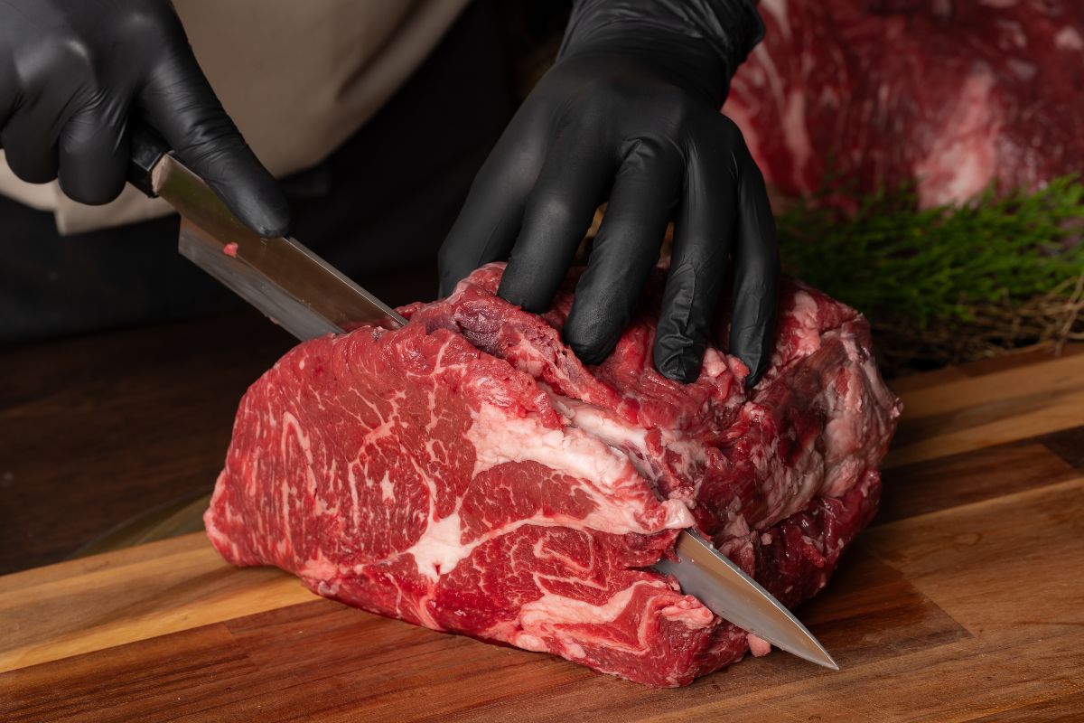 Macellaio al lavoro mentre affetta carne rossa.