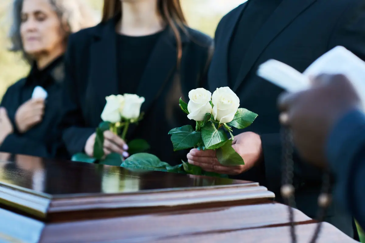 Partecipanti al funerale stringono fiori bianchi davanti alla bara.